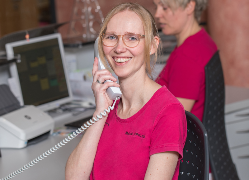 Mitarbeiterin in pinkem Shirt lacht am Telefon am Empfang