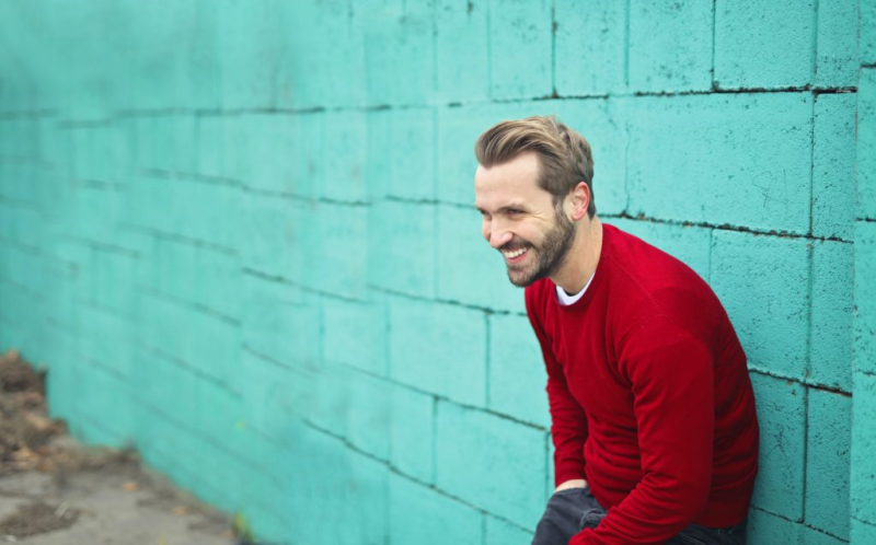 ein junger Mann steht lachend vor einer blauen Wand