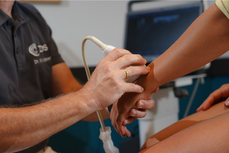 Arzt untersucht das Handgelenk einer Patientin mit einem Ultraschallgerät