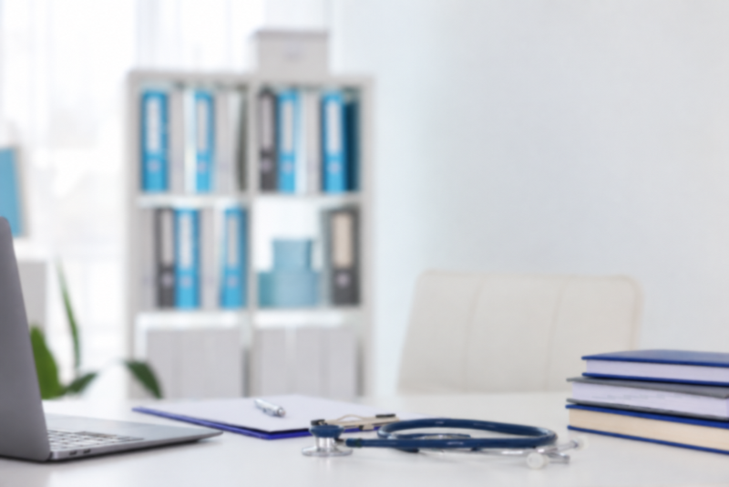 Besprechungszimmer mit Schreibtisch, Stethoskop und medizinischen Unterlagen im Hintergrund