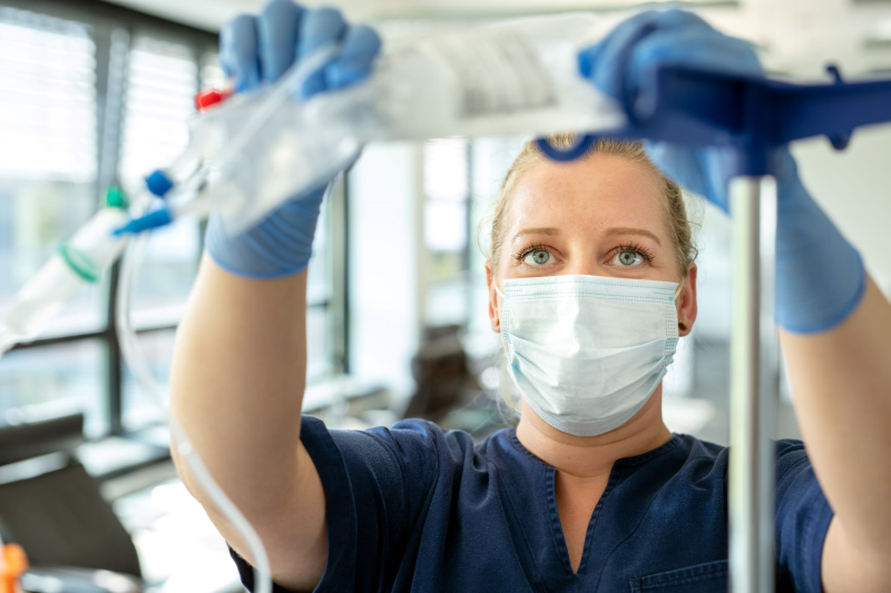 Mitarbeiterin bereitet mit blauen Handschuhen eine Infusion vor