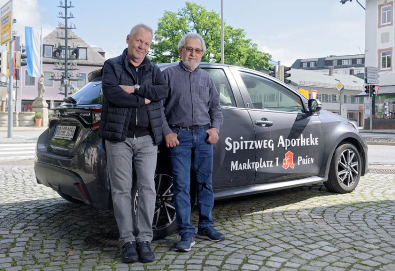 zwei Männer stehen vor einem schwarzen Auto mit dem Logo der Spitzweg-Apotheke 