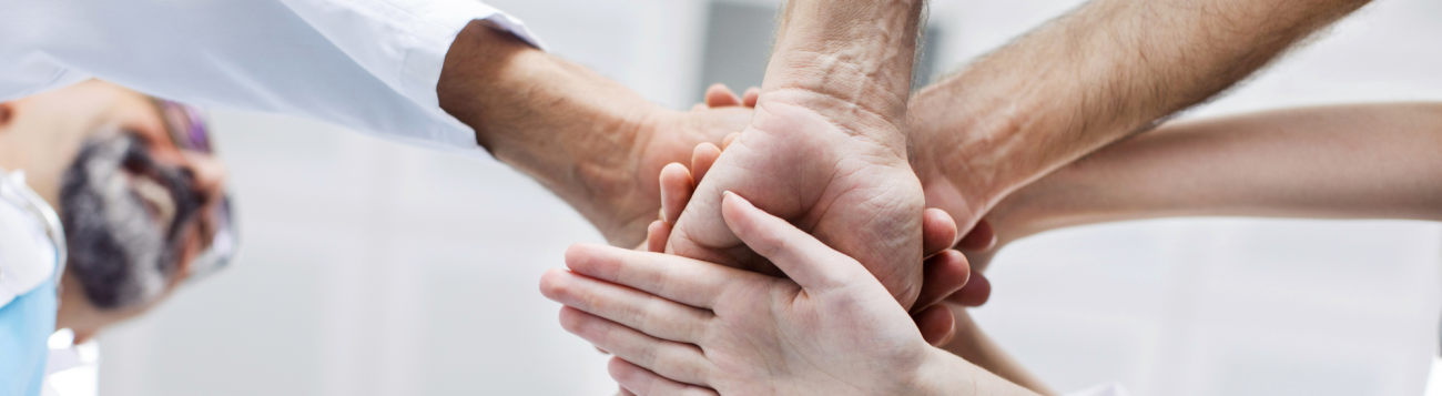 Teamwork mehrere Ärzte legen Hände aufeinander als Zeichen der Zusammenarbeit