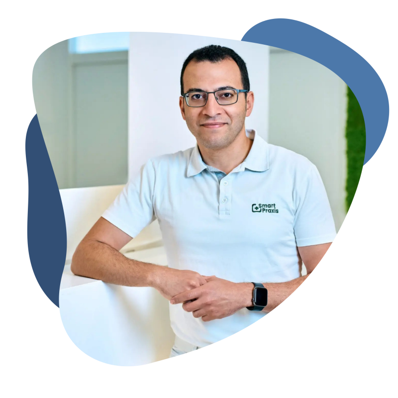 Dr. Ahmad Sirfy, Facharzt für Allgemeinmedizin Arzt mit dunklen Haaren und einer Brille in einem hellen Oberteil lehnt an einem Praxisempfang