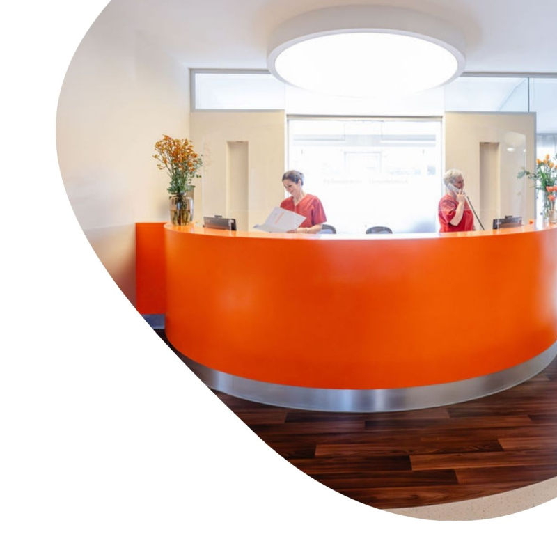 Empfang einer Arztpraxis in orange, mit zwei Mitarbeiterinnen 